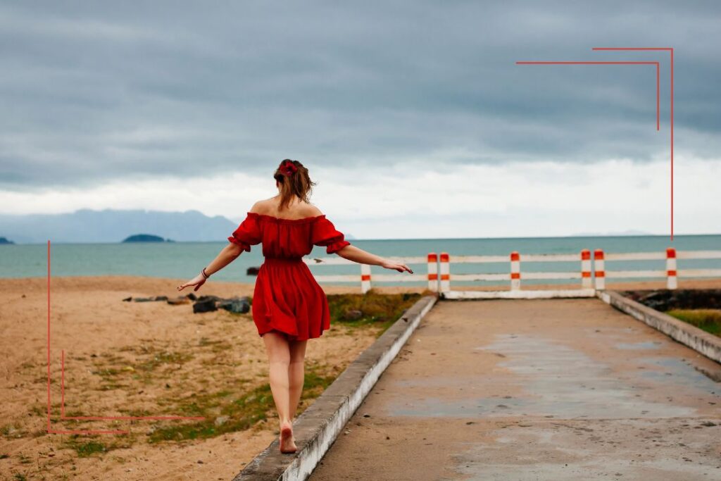 Frau im roten Kleid balanciert am Strand – Behandlung und Balance bei Östrogendominanz.